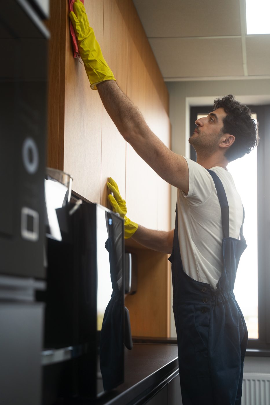 A cleaner wiping down cabinetry in a commercial kitchen