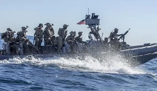 Service members in combat gear aboard a small boat flying an American flag