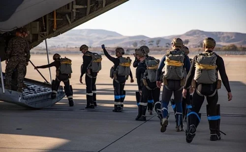Service members wearing parachute rigs walk toward the open ramp of an aircraft